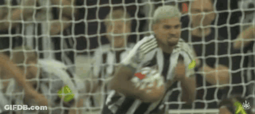 A Man In A Striped Shirt Is Holding A Soccer Ball In Front Of A Goal Net . GIF