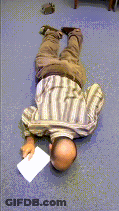 A Man In A Striped Shirt Is Laying On His Back On The Floor Holding A Piece Of Paper GIF