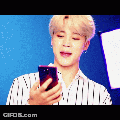 A Man In A Striped Shirt Is Looking At A Phone GIF