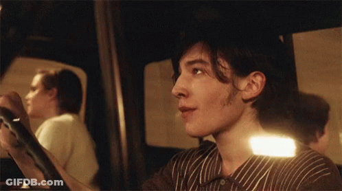 A Man In A Striped Shirt Is Looking At Something In A Mirror GIF