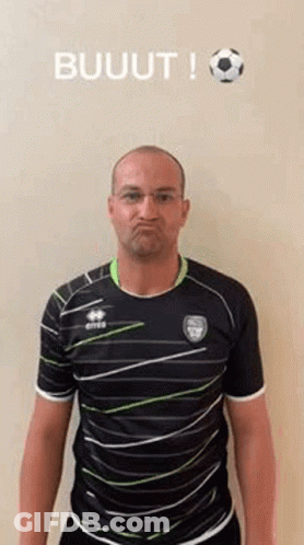 A Man In A Striped Shirt Is Making A Funny Face While Standing In Front Of A Soccer Ball . GIF