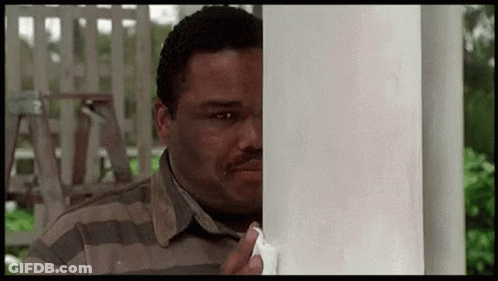 A Man In A Striped Shirt Is Peeking Around A Pole . GIF