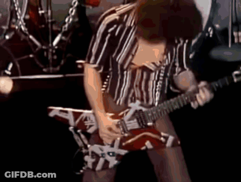 A Man In A Striped Shirt Is Playing A Guitar On Stage GIF