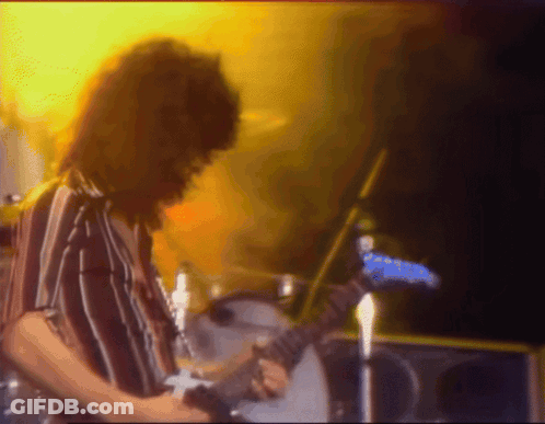 A Man In A Striped Shirt Is Playing A Guitar On Stage GIF