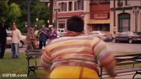A Man In A Striped Shirt Is Running In A Park In Front Of A Store That Says Sri Lankan GIF