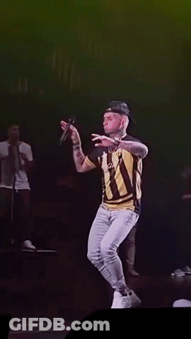A Man In A Striped Shirt Is Singing Into A Microphone On Stage GIF