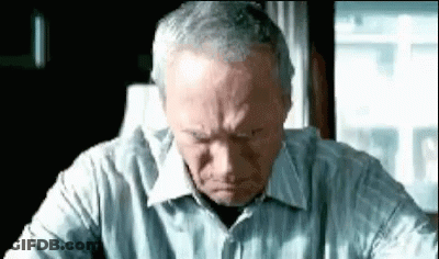 A Man In A Striped Shirt Is Sitting At A Table With His Head Down . GIF