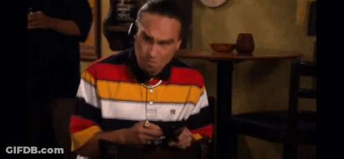 A Man In A Striped Shirt Is Sitting At A Table With The Words I 'M On It Above Him . GIF