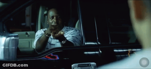 A Man In A Striped Shirt Is Sitting In A Car And Pointing At Something GIF
