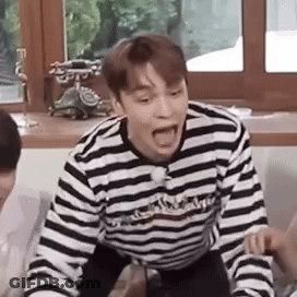 A Man In A Striped Shirt Is Sitting On A Couch With His Mouth Open And Making A Funny Face . GIF