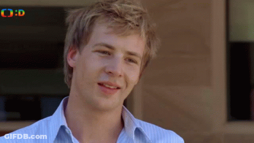 A Man In A Striped Shirt Is Smiling In Front Of A Building With The Letters O And D On The Bottom GIF