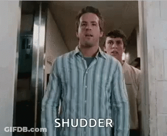A Man In A Striped Shirt Is Standing In A Hallway With Another Man Behind Him . GIF