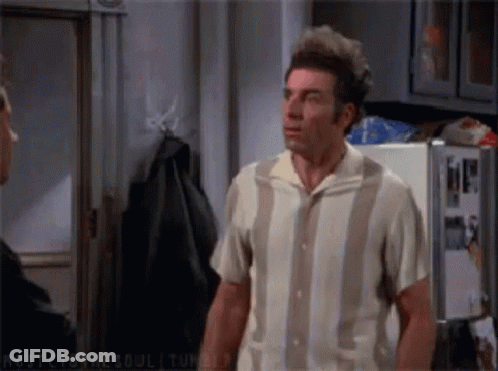 A Man In A Striped Shirt Is Standing In A Kitchen Next To A Refrigerator . GIF