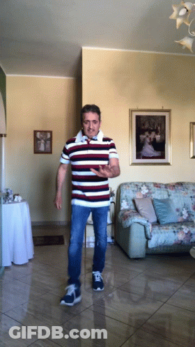 A Man In A Striped Shirt Is Standing In A Living Room In Front Of A Couch GIF