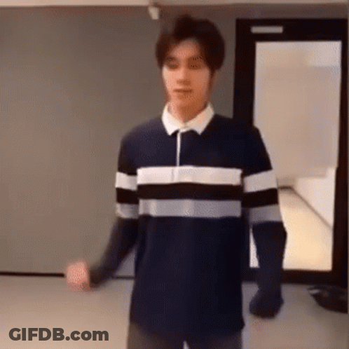 A Man In A Striped Shirt Is Standing In A Room . GIF