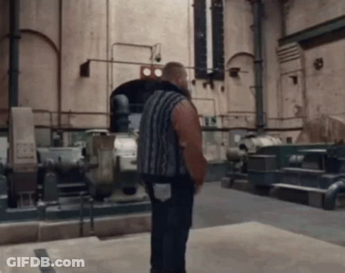 A Man In A Striped Shirt Is Standing In A Room With A Sign On The Wall That Says ' Ts ' GIF