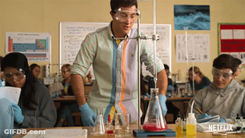 A Man In A Striped Shirt Is Standing In Front Of A Beaker With Red Liquid In It GIF