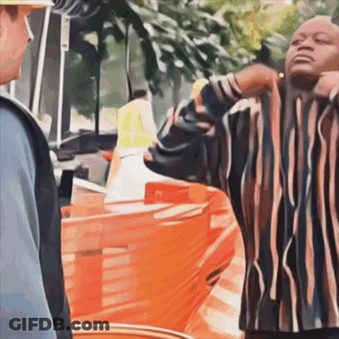 A Man In A Striped Shirt Is Standing In Front Of A Construction Site GIF