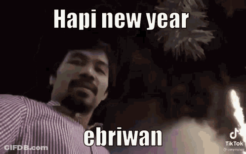 A Man In A Striped Shirt Is Standing In Front Of A Fireworks Display And Says Hapi New Year Ebriwan . GIF