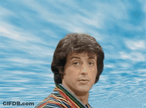 A Man In A Striped Shirt Is Standing In Front Of A Joke Sign GIF