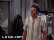 A Man In A Striped Shirt Is Standing In Front Of A Refrigerator Talking To Another Man GIF