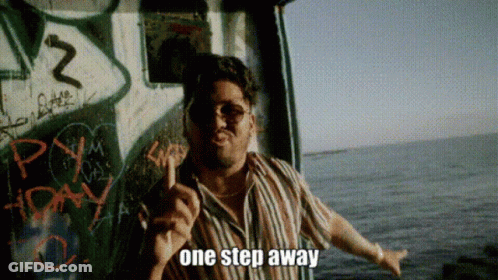 A Man In A Striped Shirt Is Standing In Front Of A Wall With Graffiti And Says One Step Away GIF