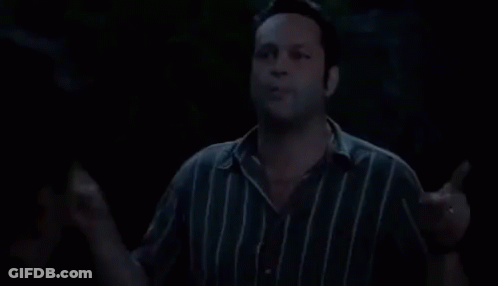 A Man In A Striped Shirt Is Standing In The Dark And Talking . GIF