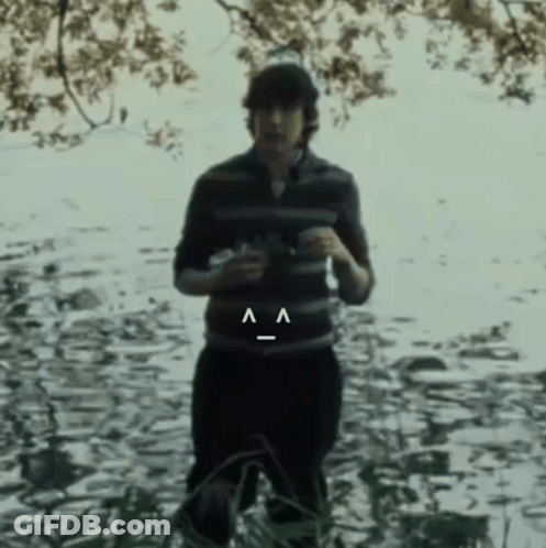A Man In A Striped Shirt Is Standing In The Water With A Smiley Face On His Belt GIF