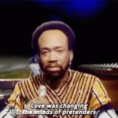 A Man In A Striped Shirt Is Talking Into A Microphone And Says `` Love Was Changing The Minds Of Pretenders '' . GIF