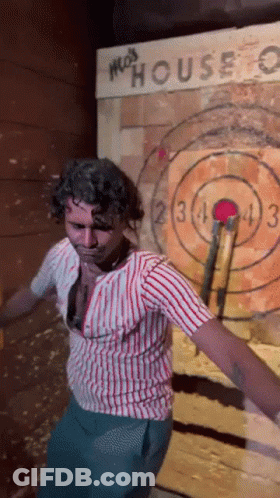 A Man In A Striped Shirt Is Throwing An Axe At A Target That Says Moss House GIF