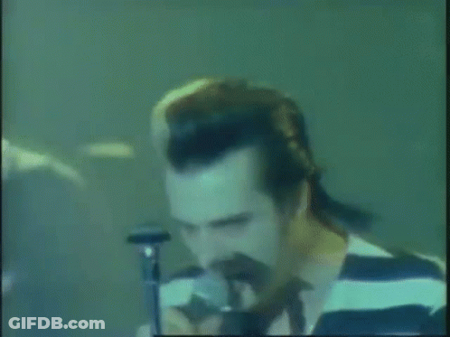 A Man In A Striped Shirt Singing Into A Microphone . GIF