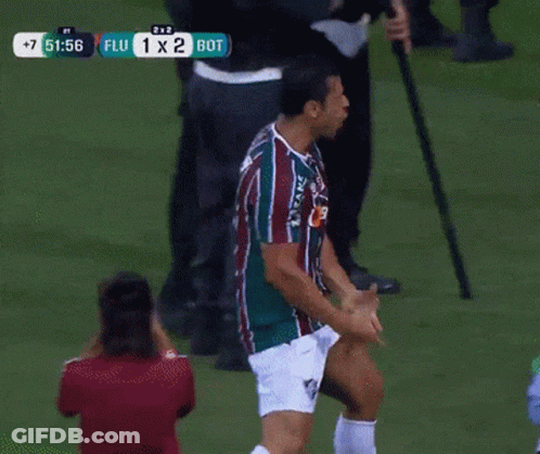 A Man In A Striped Shirt Stands On A Soccer Field With A Score Of 1 X 2 GIF