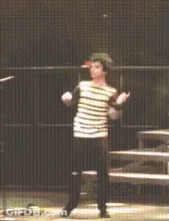 A Man In A Striped Shirt Stands On A Stage With His Arms Outstretched GIF