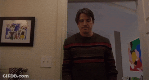 A Man In A Striped Sweater Stands In Front Of A Framed Picture On The Wall GIF