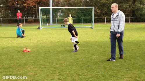 A Man In A Striped Sweatshirt Watches A Boy Kick A Soccer Ball GIF