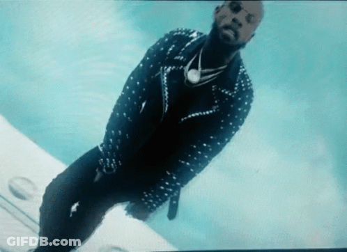 A Man In A Studded Jacket And Sunglasses Is Standing On A Plane GIF
