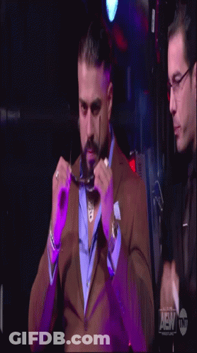 A Man In A Suit Adjusts His Glasses While Another Man Looks On GIF