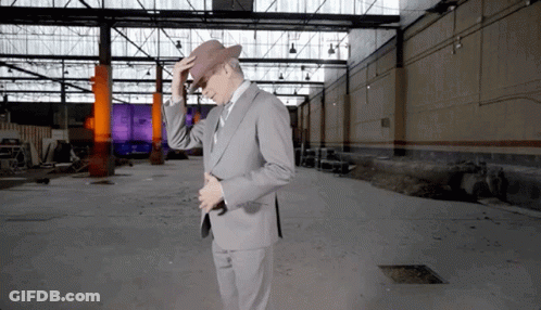 A Man In A Suit Adjusts His Hat In An Empty Building GIF