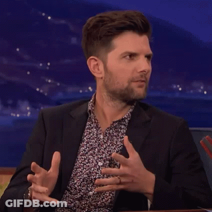 A Man In A Suit And A Floral Shirt Is Making A Funny Face While Sitting At A Table . GIF