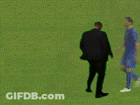 A Man In A Suit And A Man In A Blue Shirt Are Standing On A Green Field GIF