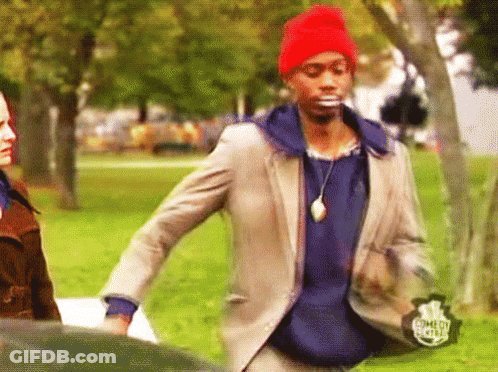 A Man In A Suit And A Red Hat Is Standing In A Park With A Comedy Central Logo On His Jacket GIF