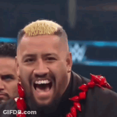 A Man In A Suit And A Red Lei Is Laughing . GIF