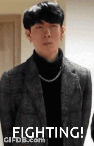 A Man In A Suit And A Turtleneck Is Standing In Front Of A Sign That Says Fighting ! GIF