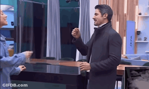 A Man In A Suit And A Woman In A Blue Jacket Are Standing In A Room . GIF