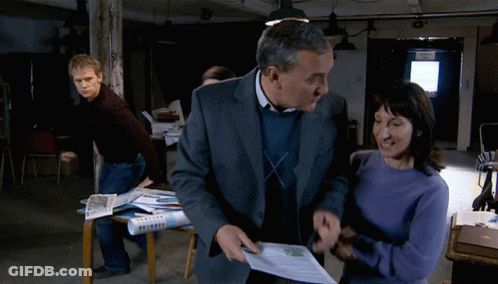 A Man In A Suit And A Woman In A Blue Sweater Are Standing In Front Of A Door That Says ' Exit ' GIF