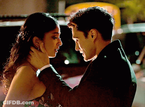 A Man In A Suit And A Woman In A Dress Are Looking At Each Other GIF