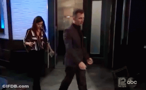 A Man In A Suit And A Woman In A Striped Shirt Are Walking Through A Doorway On Abc . GIF