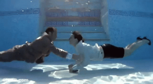 A Man In A Suit And A Woman In A White Shirt Are Underwater In A Swimming Pool GIF