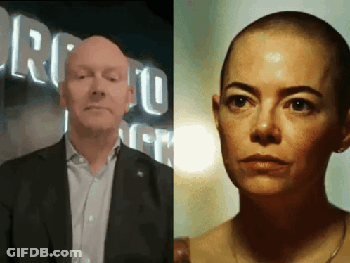 A Man In A Suit And A Woman With A Shaved Head In Front Of A Sign That Says Toronto GIF