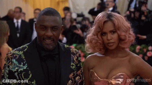 A Man In A Suit And A Woman With Pink Hair Pose For A Photo GIF